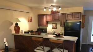 A kitchen with wooden cabinets, a black refrigerator, a microwave, and a bar stool. - Awesome condo, great location, quiet area, completely updated, with wifi.& AC (Ruidoso)