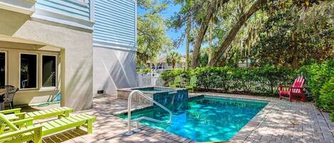 Un área de piscina con una piscina azul cristalina, sillas de lounge de madera y un patio de ladrillo.
