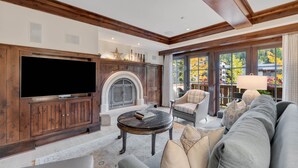A living room with a fireplace, a television, and a large window with a view of trees. - One Willow Bridge Road - 3-room residence (Vail)