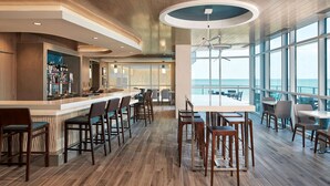 A modern bar area with wooden flooring, bar stools, and a counter with a view of the sea.