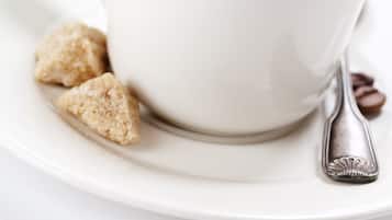 A white cup of coffee on a saucer with a spoon, accompanied by a bowl of fruit and a croissant.