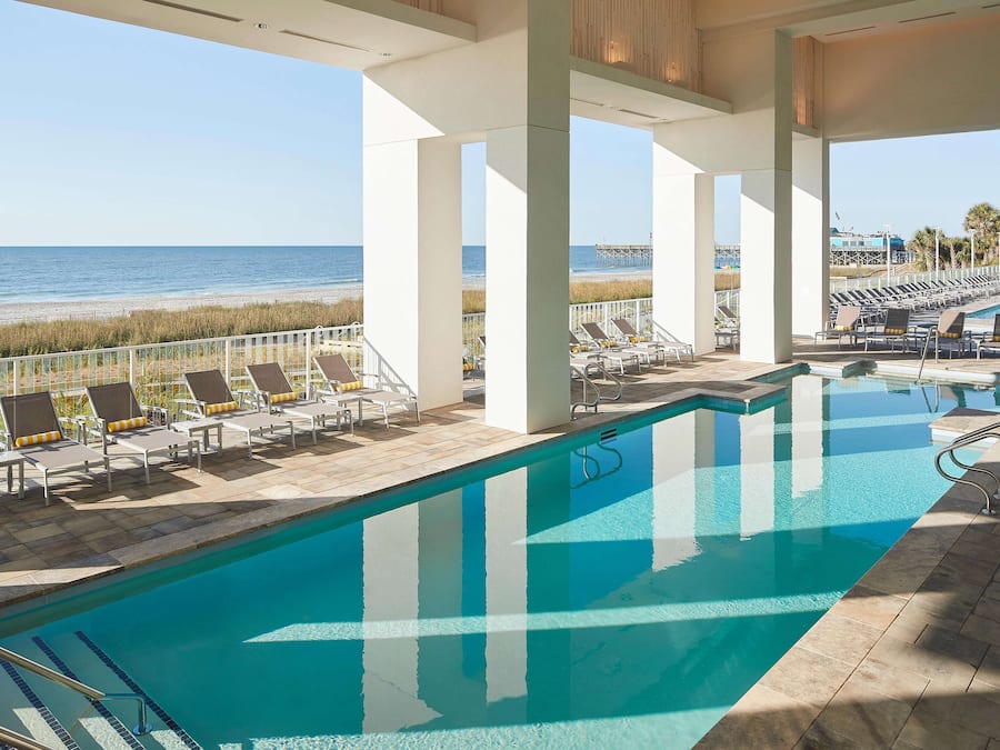 A pool area with lounge chairs and a view of the beach.