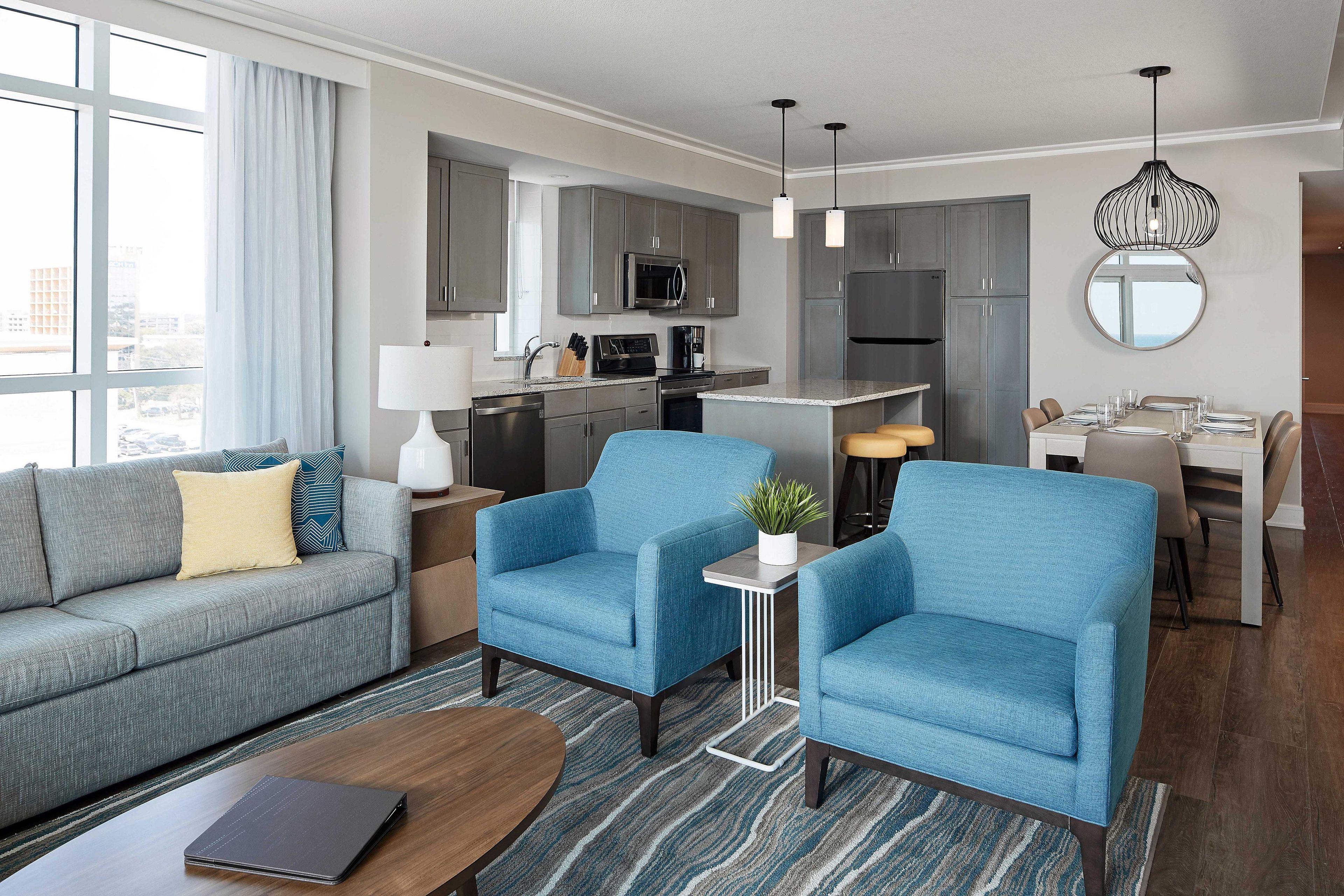 A modern living room with a sofa, two armchairs, a coffee table, and a dining area with a table set for four.