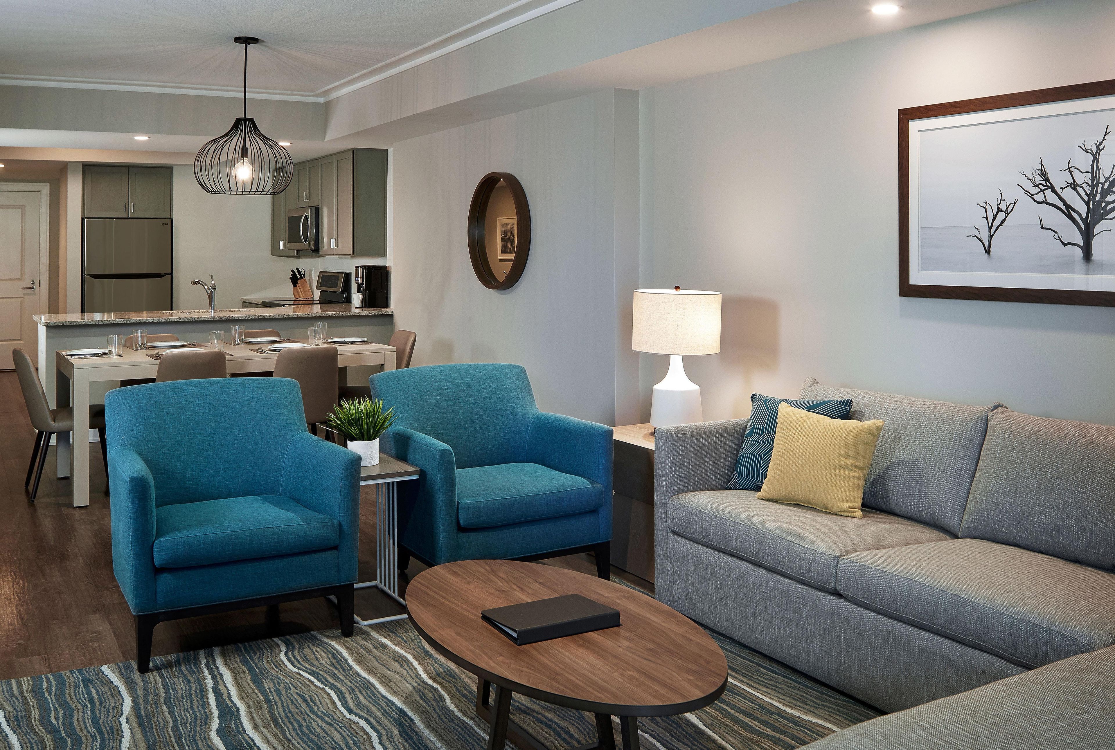 A modern living room with a grey sofa, two blue armchairs, a coffee table, and a dining area with a kitchen in the background.