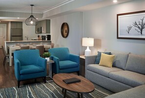 A modern living room with a grey sofa, two blue armchairs, a coffee table, and a dining area with a kitchen in the background. - Hilton Grand Vacations Club Ocean Enclave Myrtle Beach (Myrtle Beach)
