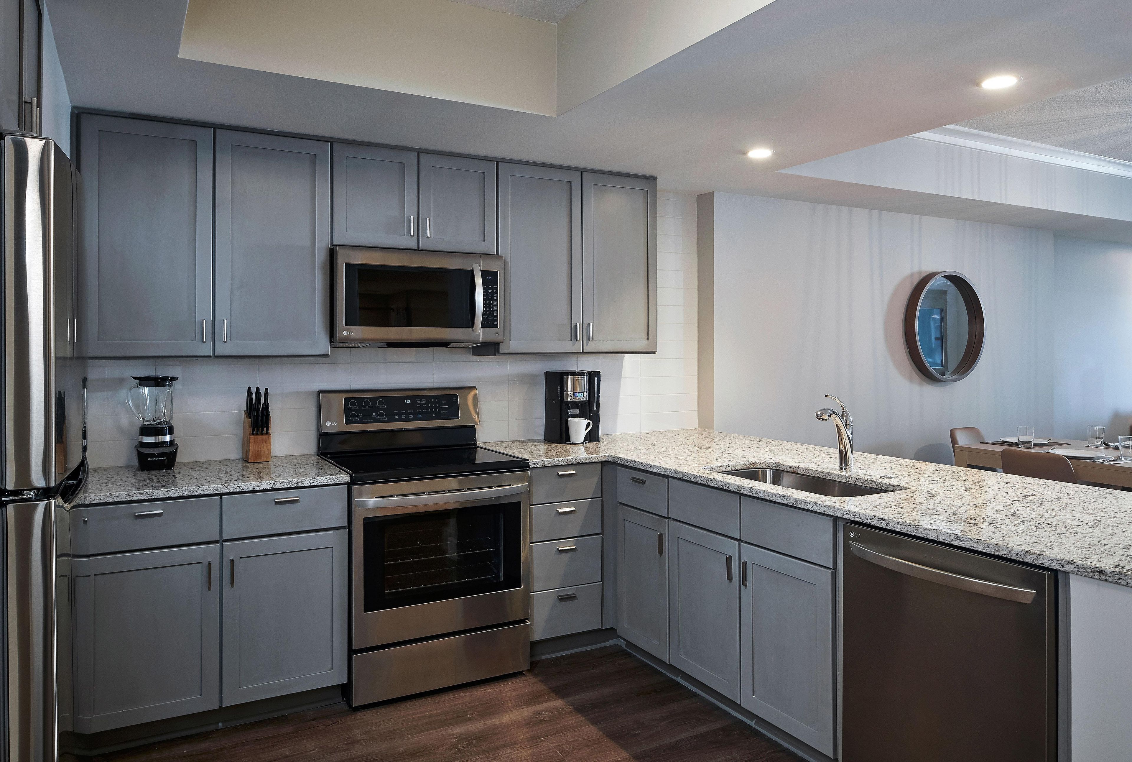 A modern kitchen with stainless steel appliances, grey cabinetry, and a granite countertop.