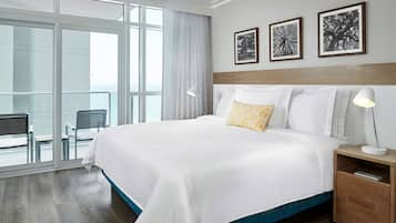 Habitación de hotel con una cama grande, una mesita de noche, una lámpara y vistas al balcón.