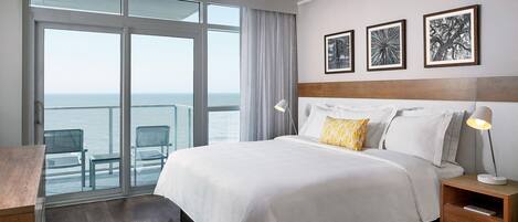 Ein Hotelzimmer mit einem großen Bett, einem Nachttisch, einem Schreibtisch und Blick auf den Ozean.