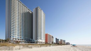 A high-rise hotel with multiple floors, a beach in the background, and a clear sky. - Hilton Grand Vacations Club Ocean Enclave Myrtle Beach (Myrtle Beach)