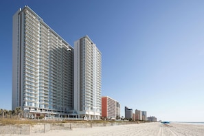 A high-rise hotel with multiple floors, a beach in the background, and a clear sky. - Hilton Grand Vacations Club Ocean Enclave Myrtle Beach (Myrtle Beach)