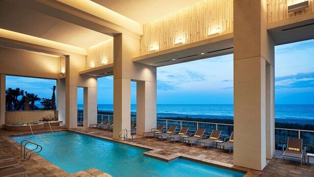 An indoor swimming pool with lounge chairs and a view of the ocean.