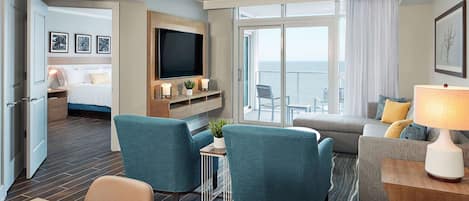 A hotel room with a bed, a TV, a seating area with chairs, a sofa, and a view of the ocean.