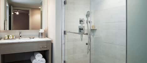 A modern bathroom with a glass-enclosed shower, a vanity with a mirror, and a shelf with towels.