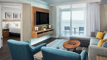 A modern hotel room with a balcony, a sofa, two armchairs, a TV, and a bed.