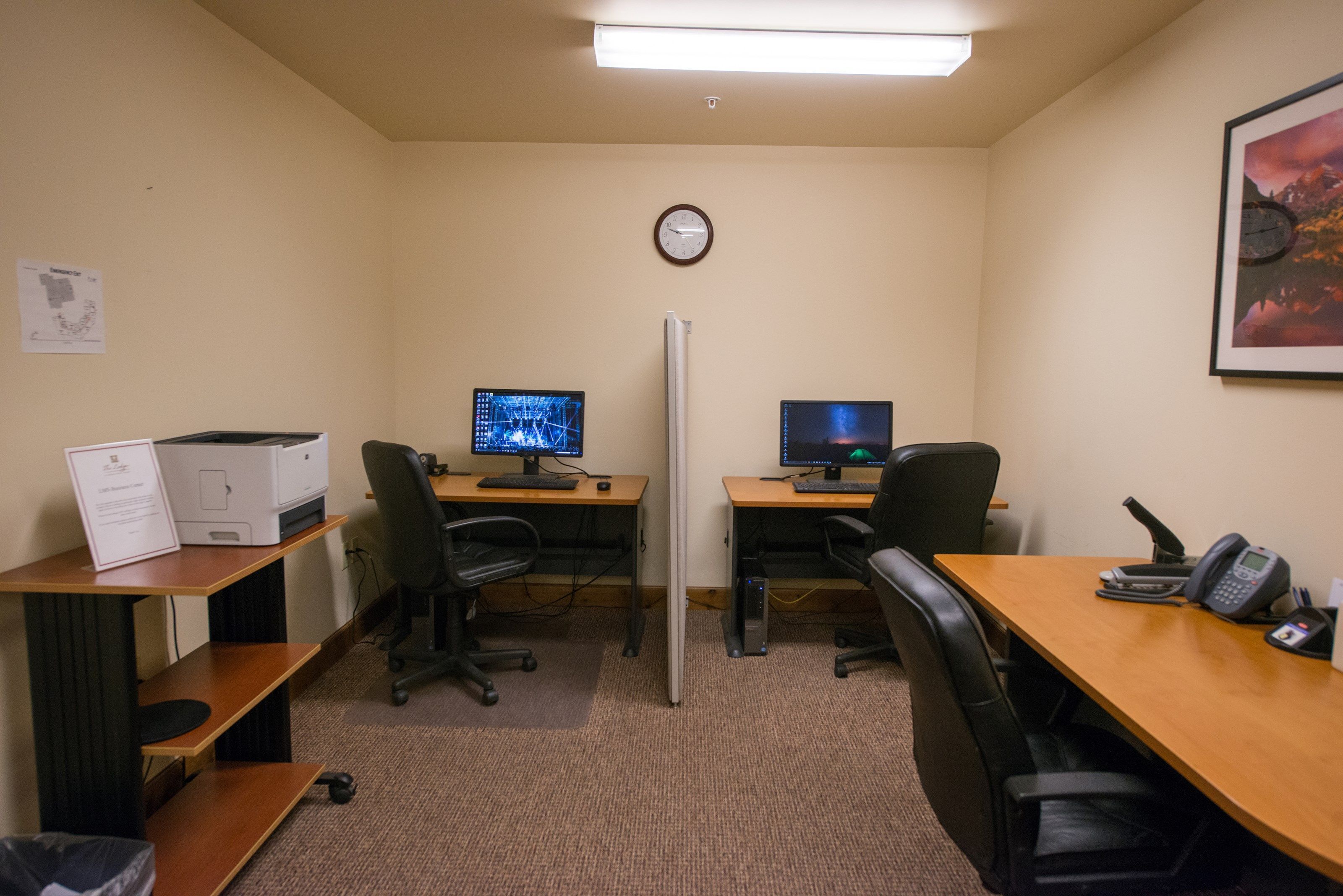 A conference room with two desks, chairs, a clock, and a refrigerator.