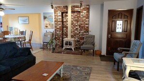 Een woonkamer met een bakstenen muur, een open haard, een eethoek met een tafel en stoelen, en een deur met een raam.
