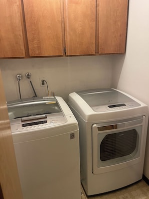 A laundry area with two washing machines and a dryer, wooden cabinets above, and a tiled floor.