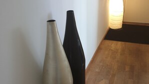 Zwei Vasen, eine beige und eine schwarz, stehen an einer weißen Wand in einer Ecke mit Holzboden.