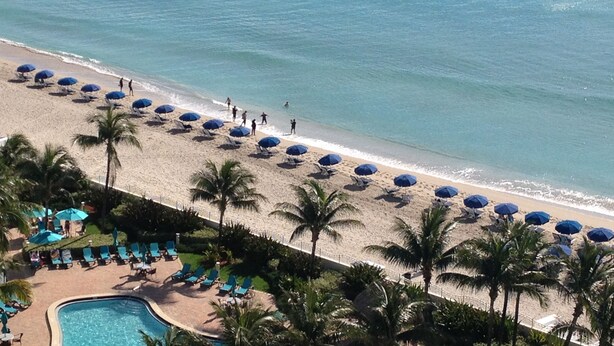 A beach resort with a pool, sun loungers, and umbrellas. - Sunrise+Sunset on the Beach  (Hollywood)