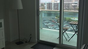 A hotel room with a large sliding glass door leading to a balcony with a view of a parking area and buildings. - Sunrise+Sunset on the Beach  (Hollywood)