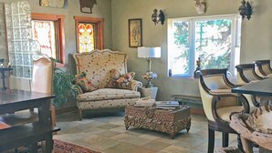 Una sala de estar con una mesa de comedor, un sofá y una mesa de centro. Hay ventanas con cortinas, un candelabro y decoración en las paredes.