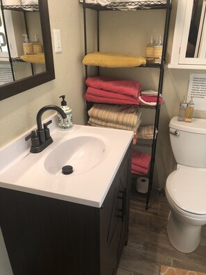A bathroom with a white sink, black faucet, and a mirror above it. There are shelves with towels and toiletries.