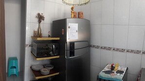 Cocina compacta con refrigerador de acero inoxidable, microondas y horno pequeño. Hay estantes con vajilla y un taburete.