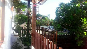 Una cerca de madera con plantas trepadoras, un portón metálico y un edificio al fondo.