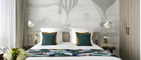 A hotel room with a bed, a nightstand, a lamp, a vase with flowers, and a wall mural of hot air balloons.