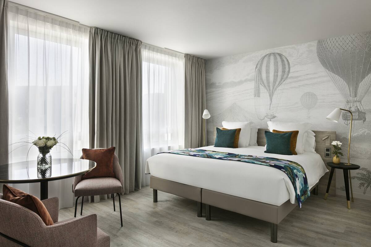 A modern hotel room with a large bed, a round dining table, and a view of hot air balloons on the wall.