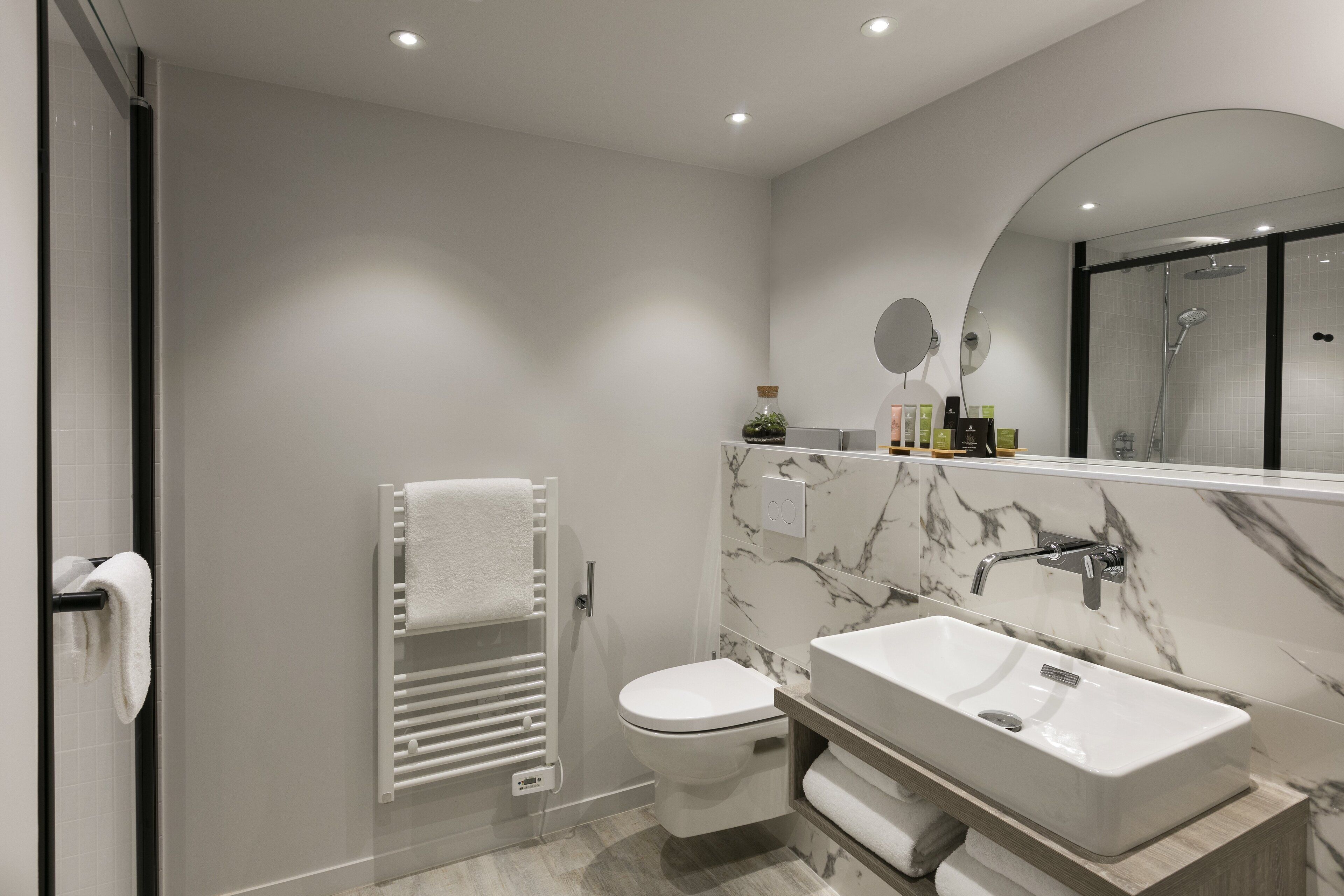 Un baño moderno con inodoro blanco, lavamanos rectangular y ducha con mampara de vidrio.