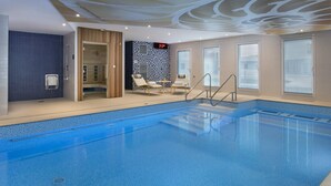 A modern indoor swimming pool with clear blue water, a digital clock, and a seating area with chairs and a table. - Citadines Confluent Nantes (Nantes)