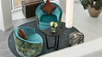 A modern interior with teal armchairs, a small round table, and a decorative vase.