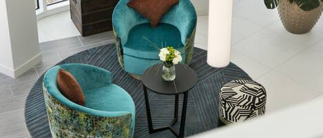 A modern interior with teal armchairs, a small round table, and a decorative vase.