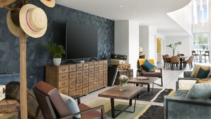 A modern living room with a large flat-screen TV, a wooden cabinet with drawers, a sofa, a coffee table, and a dining area with chairs and a table. - Citadines Confluent Nantes (Nantes)