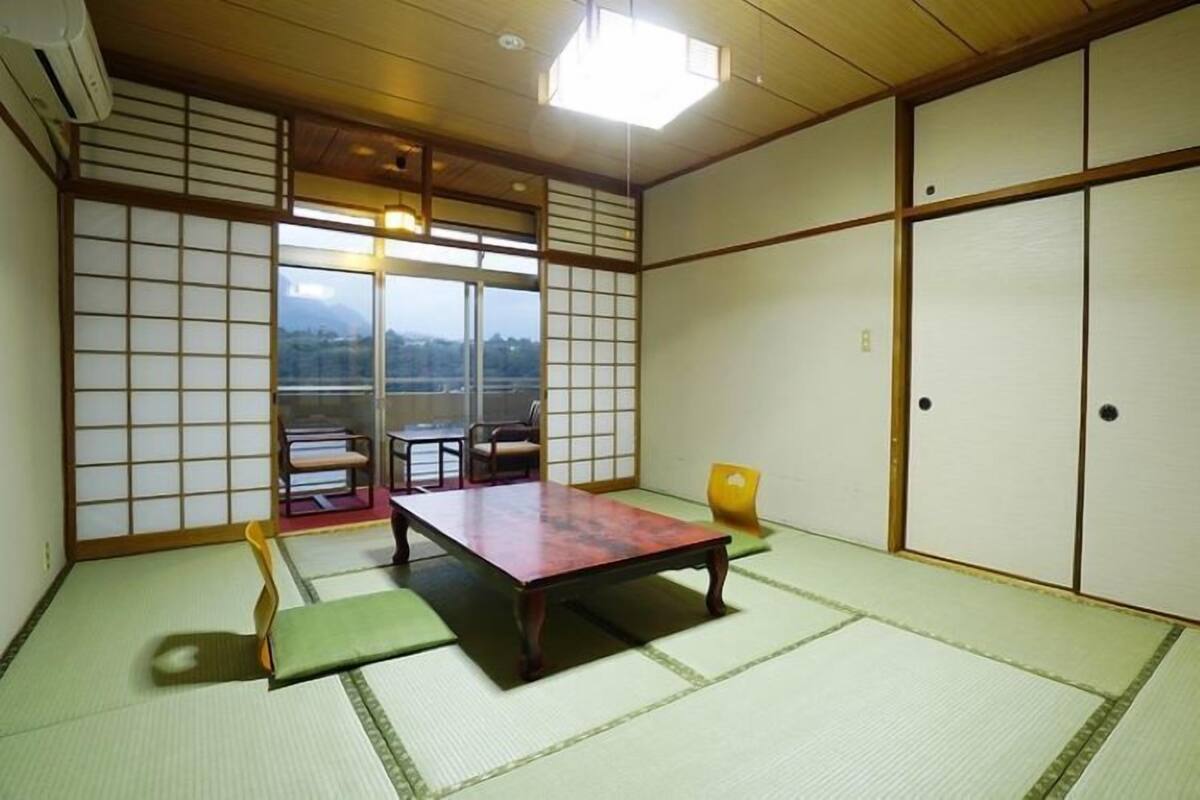 Ett traditionellt japanskt rum med tatamimattor på golvet, ett lågt bord, en stol och skjutdörrar.