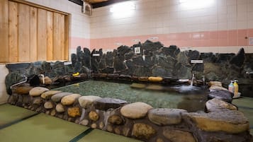 Un onsen japonés tradicional con pared de piedra, fuente termal y suelo de baldosas.