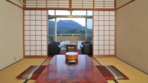 Ein traditioneller japanischer Raum mit Tatami-Bodenbelag, einem niedrigen Tisch mit Kissen und Blick auf einen Berg.