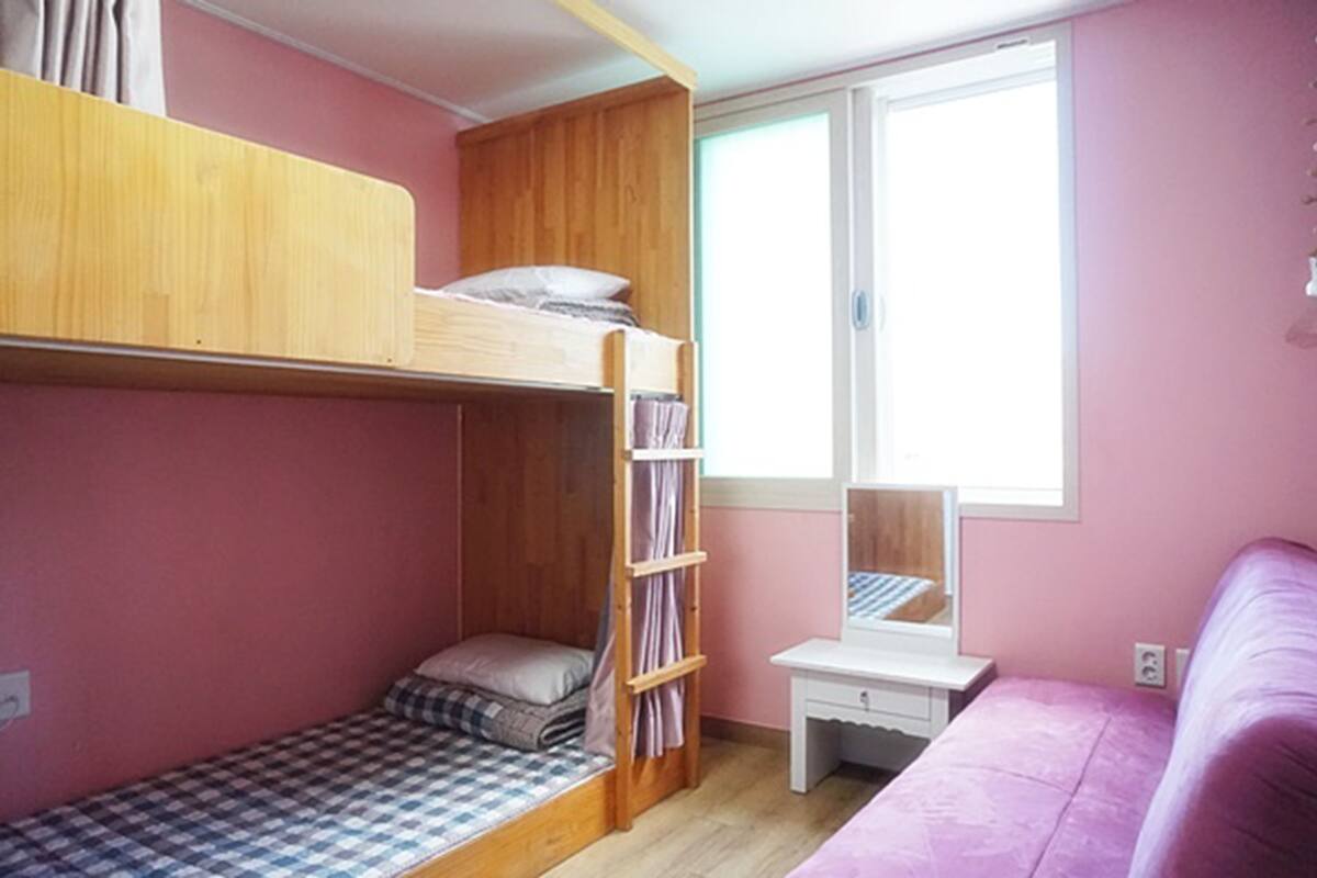 Un dormitorio con literas, un escritorio pequeño, una ventana y una cama rosa.