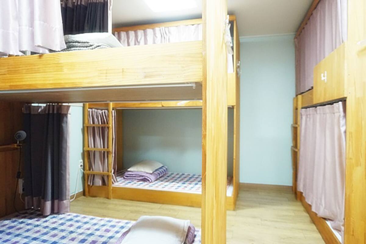 Un dormitorio con literas, un armario pequeño y una ventana con cortinas.