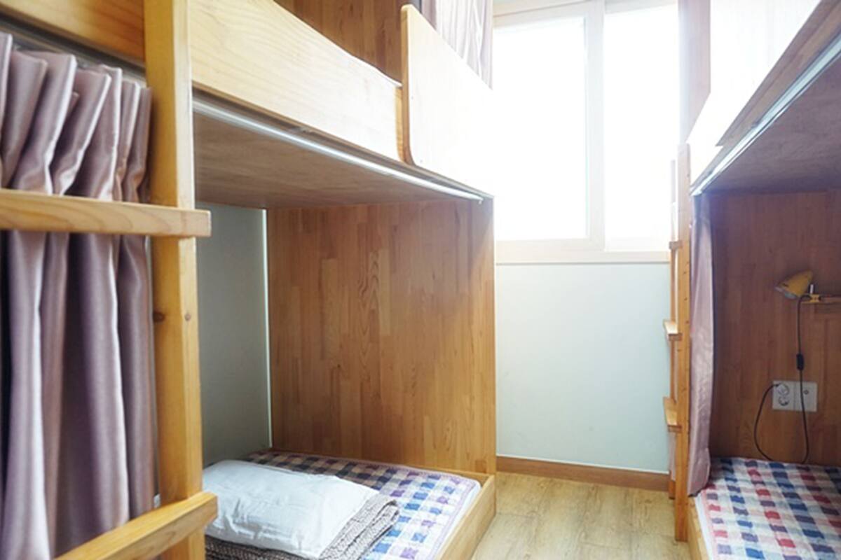 Habitación pequeña con dos literas, paredes de madera, una ventana y un enchufe a la vista.