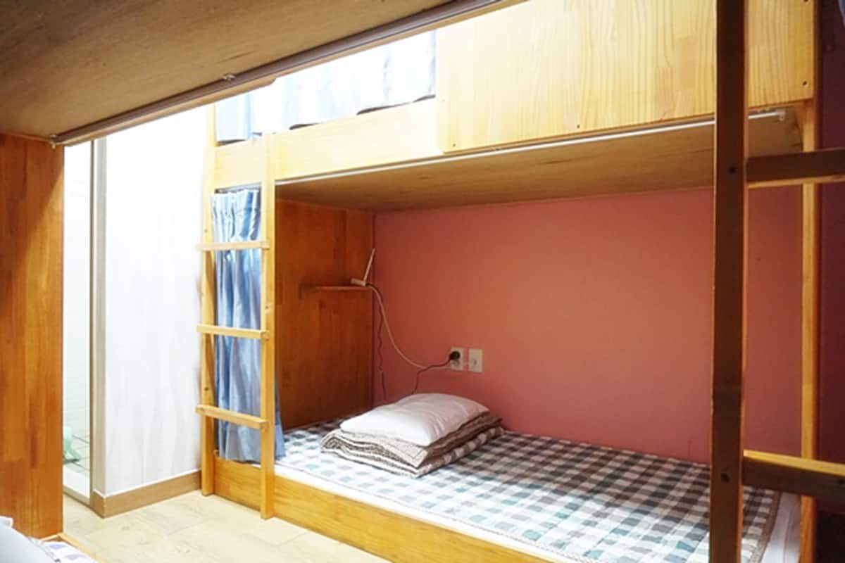 Una habitación pequeña con una cama litera, una ventana con cortinas y un enchufe.