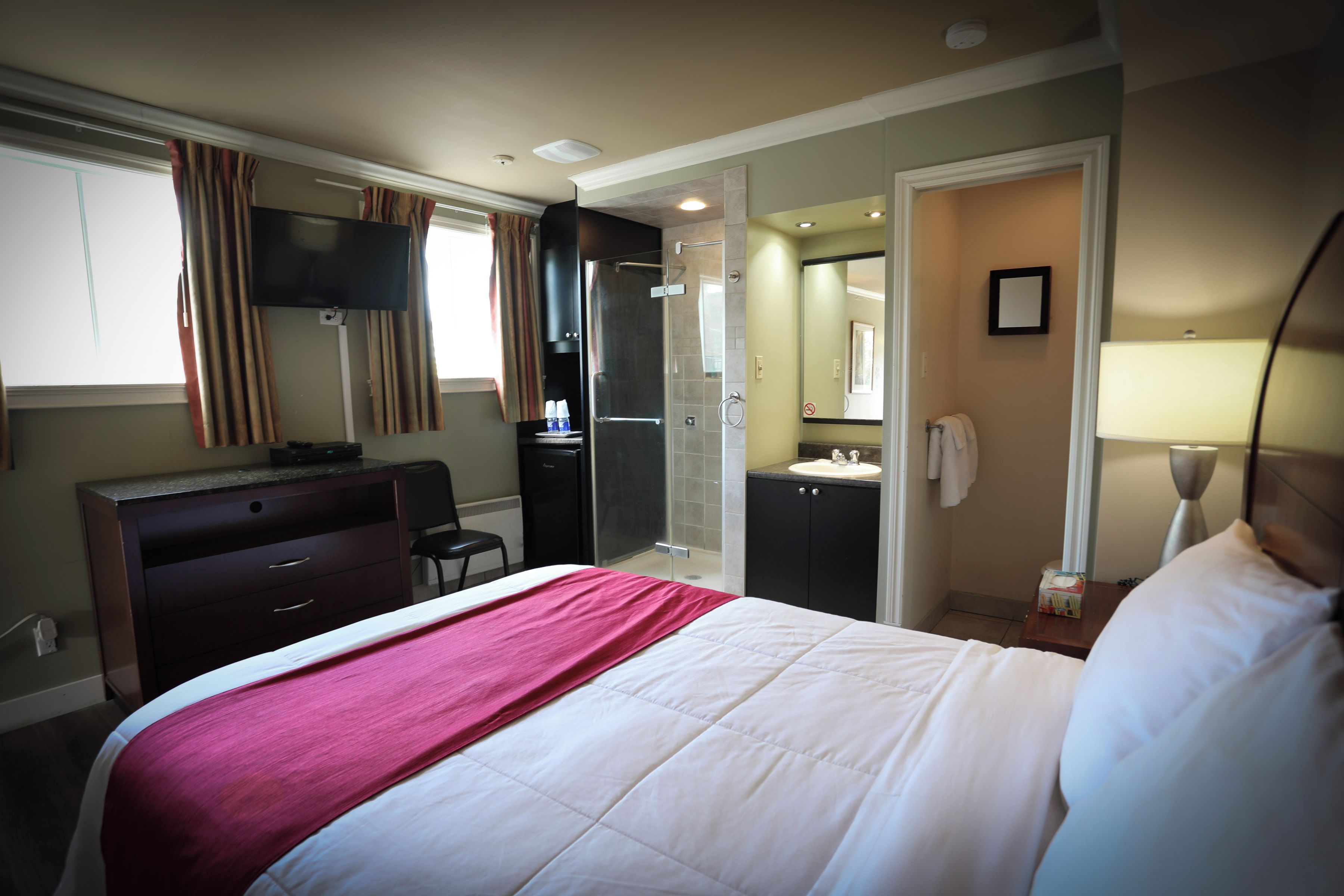 A hotel room with a bed, a desk, a television, a wardrobe, a bathroom with a mirror, and a shower.