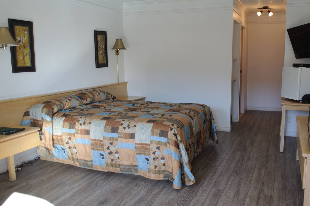 A bedroom with a bed, bedside table, lamp, desk with a computer, and a TV.