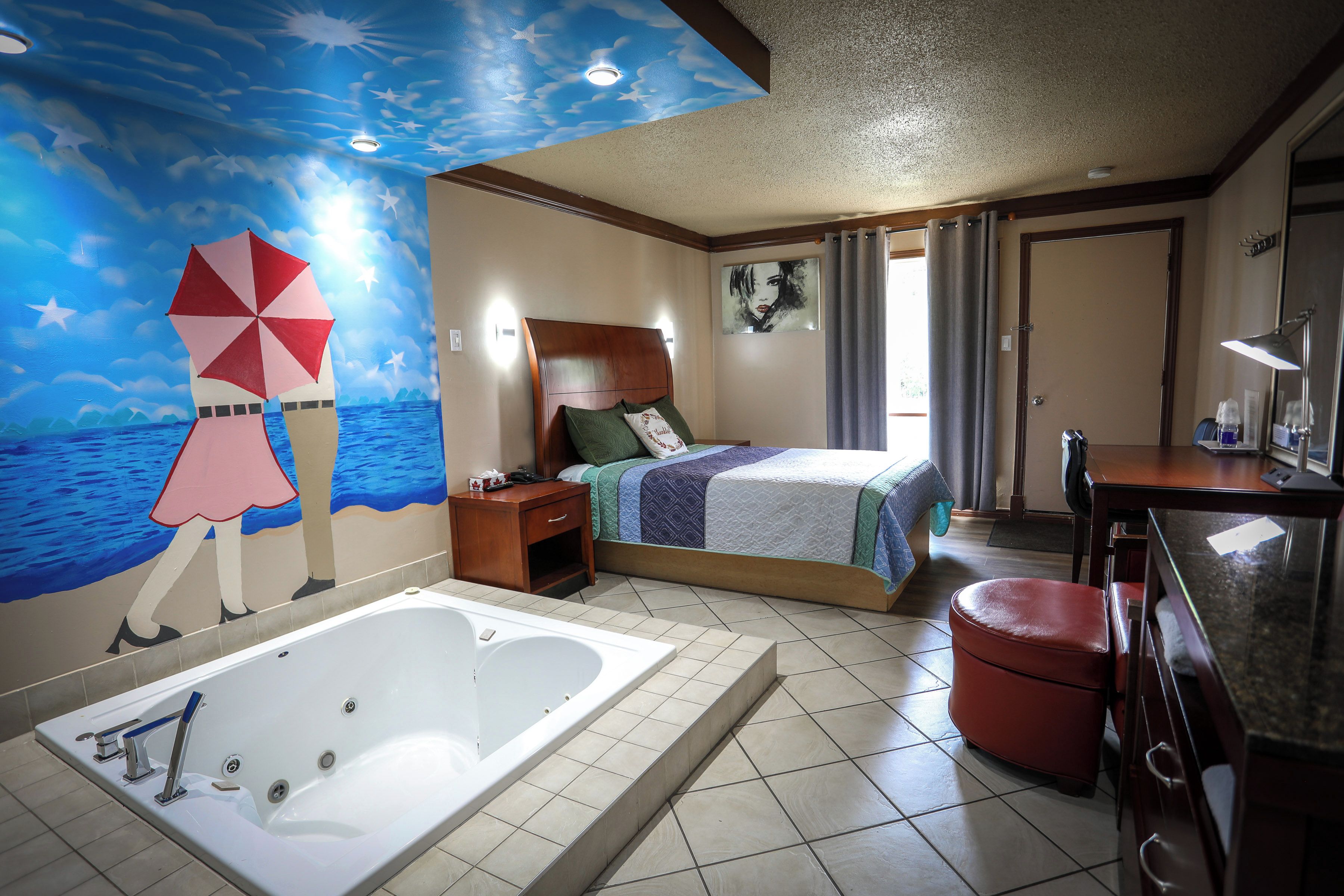 A hotel room with a large bed, a separate bathroom with a bathtub, a ceiling mural, and a window with curtains.