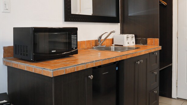 A compact kitchen with a microwave, toaster, sink, and dark cabinets. - Motel LeClassique (Saint-Charles-Borromée)