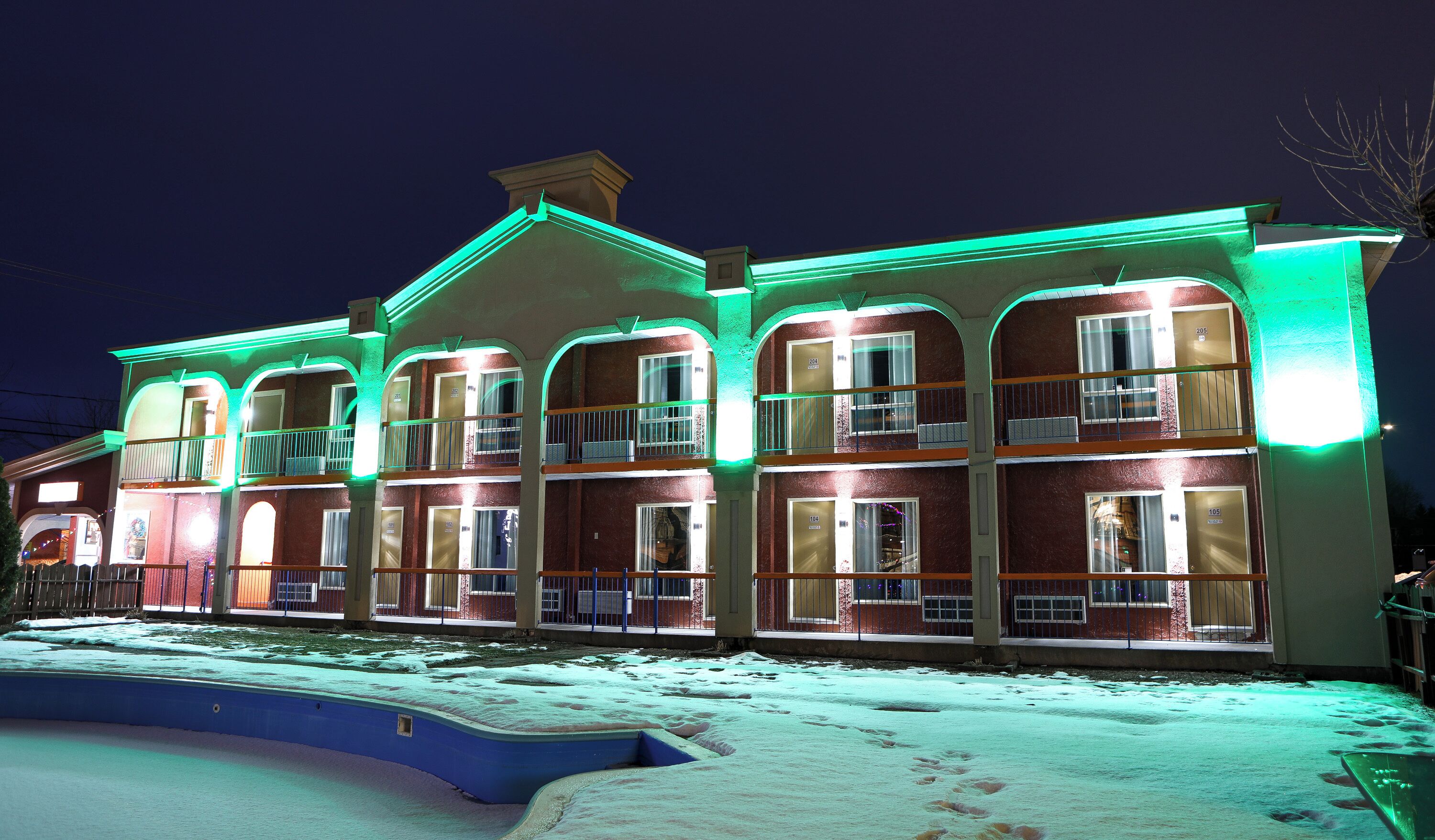 A multi-story building with balconies, a swimming pool, and a snow-covered ground.