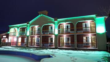 A multi-story building with balconies, a swimming pool, and a snow-covered ground.