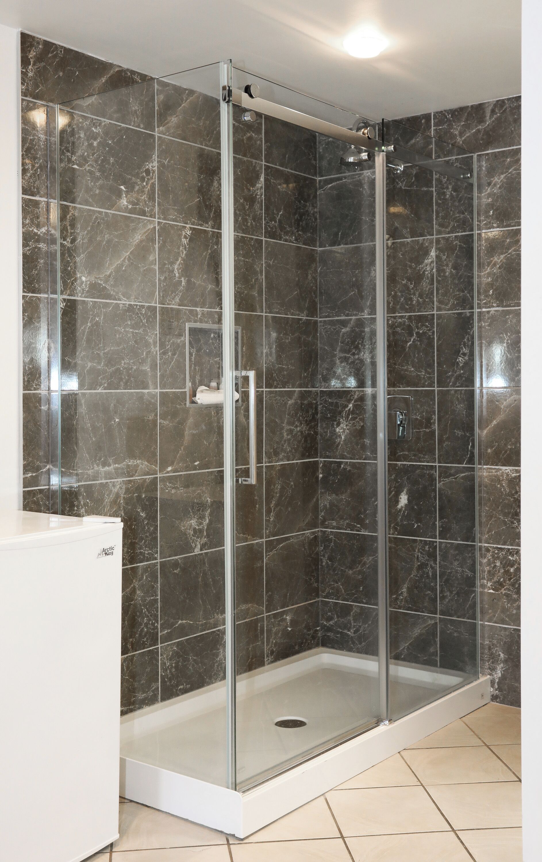 Une cabine de douche fermée par des parois en verre, avec un receveur blanc et un mur recouvert de carreaux de marbre.