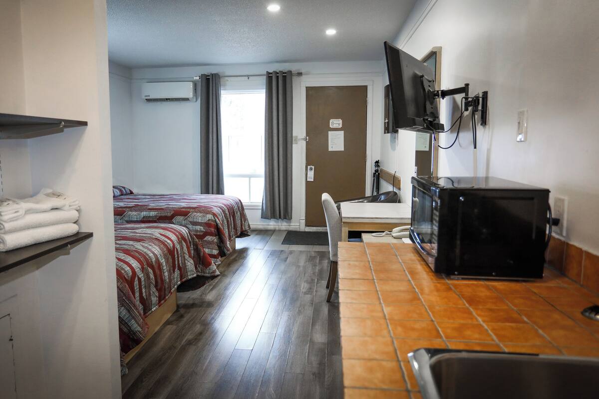 A hotel room with two beds, a TV, a desk with a computer, a chair, and a shelf with towels.